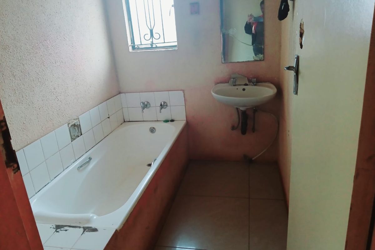 A dated bathroom featuring a standard bathtub, wall-mounted basin, and tiled flooring, requiring cosmetic updates and repairs to the wall finishes and fixtures.