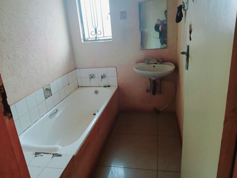A dated bathroom featuring a standard bathtub, wall-mounted basin, and tiled flooring, requiring cosmetic updates and repairs to the wall finishes and fixtures.
