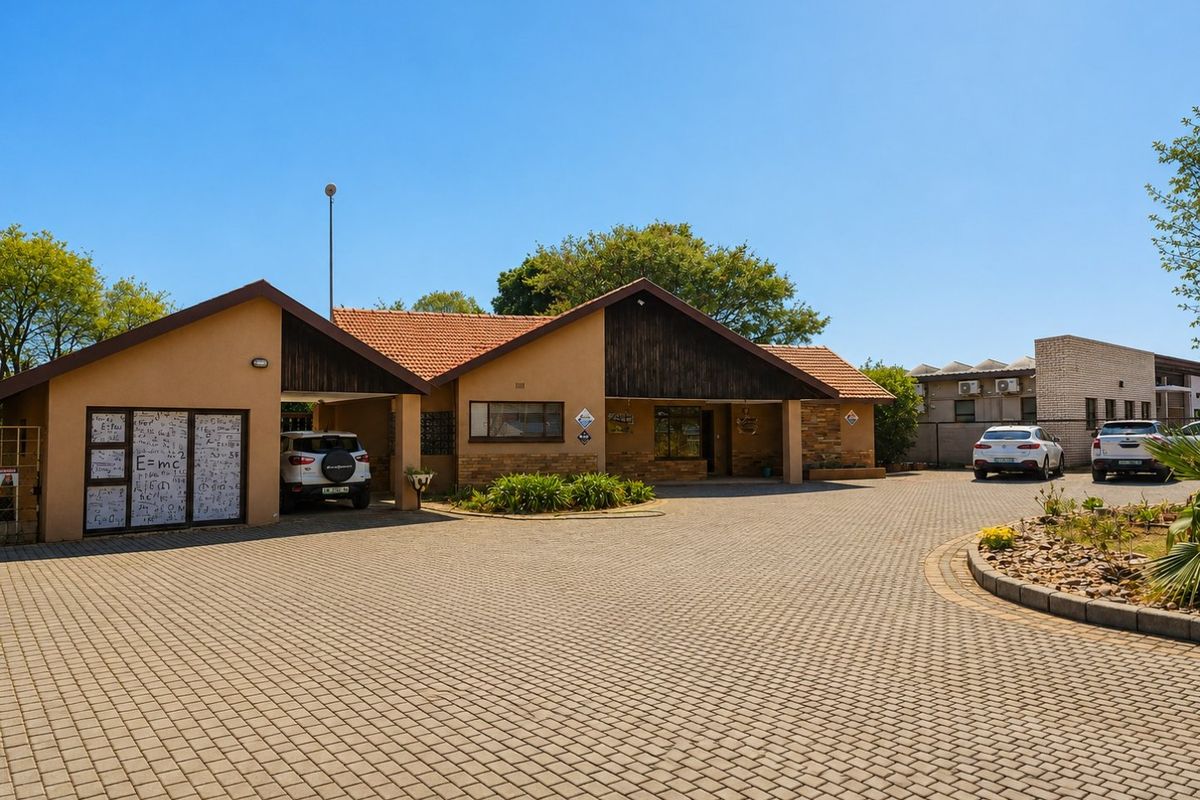Front exterior view of a commercial property featuring a large paved driveway, carport, and a combination of stone and timber facade finishes.