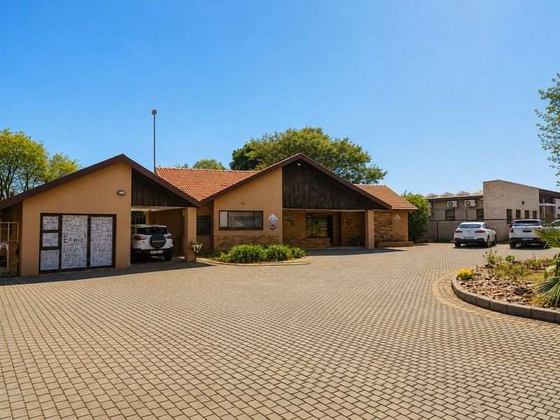 Front exterior view of a commercial property featuring a large paved driveway, carport, and a combination of stone and timber facade finishes.