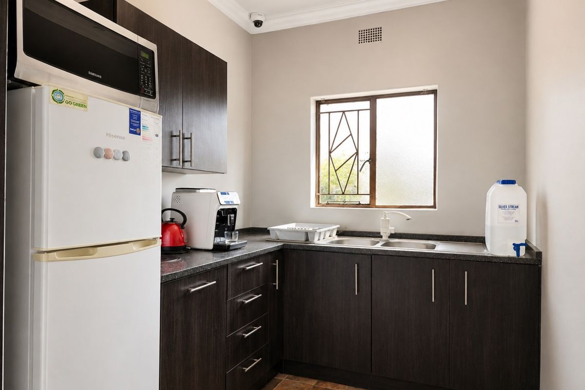A functional kitchen featuring dark wood-finish cabinetry, laminate countertops, a double stainless steel sink, and a built-in microwave, complemented by a secure window.