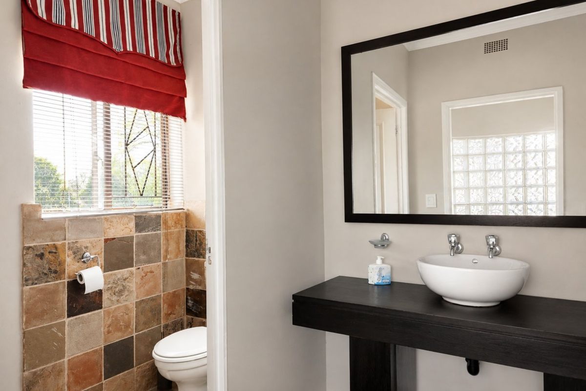 A modern bathroom featuring a floating vanity with a vessel sink, framed mirror, and a separate toilet area with slate tile accents.