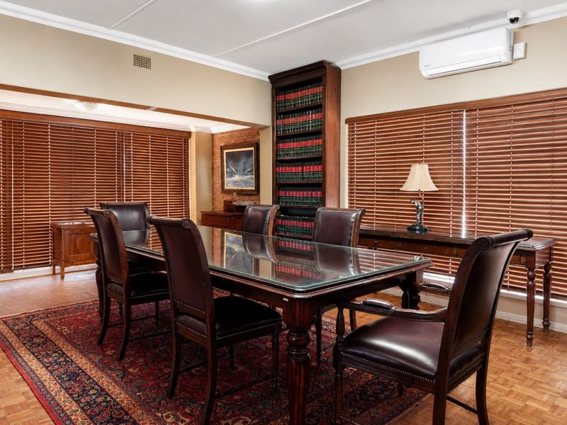 A professional office space featuring parquet flooring, a built-in bookshelf, split-system air conditioning, and large windows with venetian blinds.