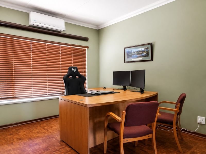 A functional office space featuring parquet flooring, a wall-mounted air conditioning unit, and venetian blinds for light control.