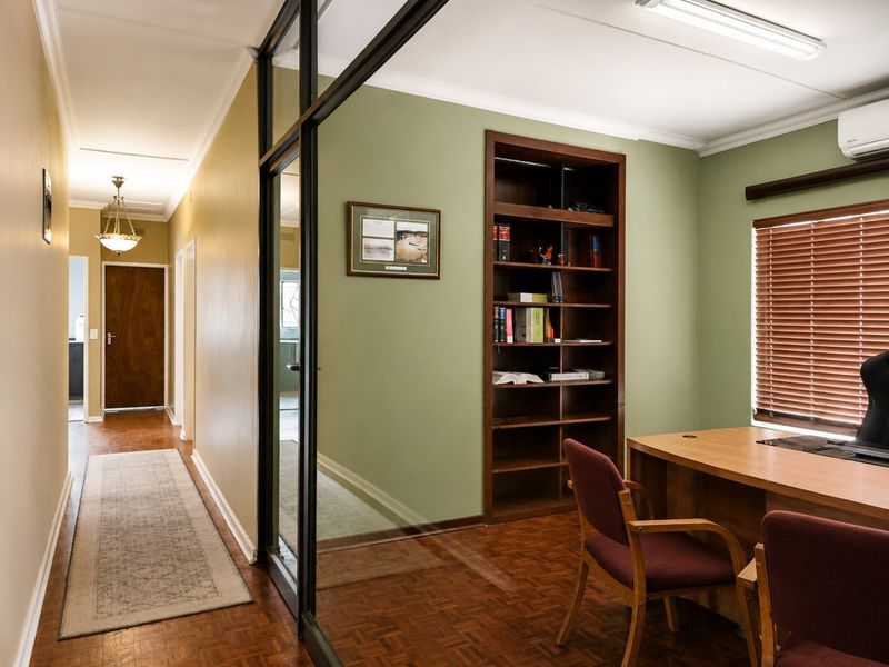 A professional office space featuring parquet flooring, built-in wooden shelving, and a glass partition wall, complemented by a split-system air conditioner.