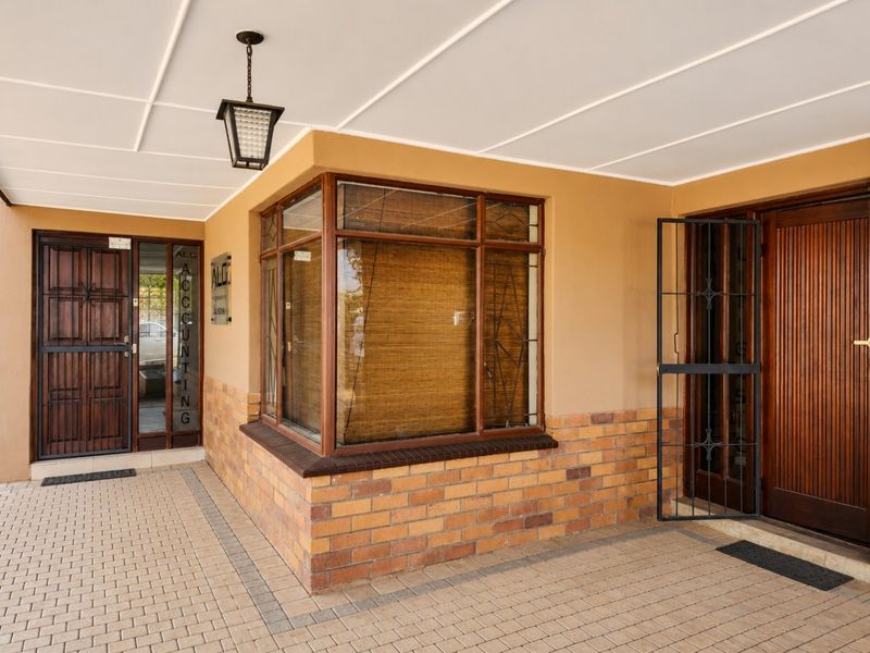 A well-maintained commercial entrance featuring a covered walkway, brick facade, timber-framed windows, and secure timber doors with metal security gates.