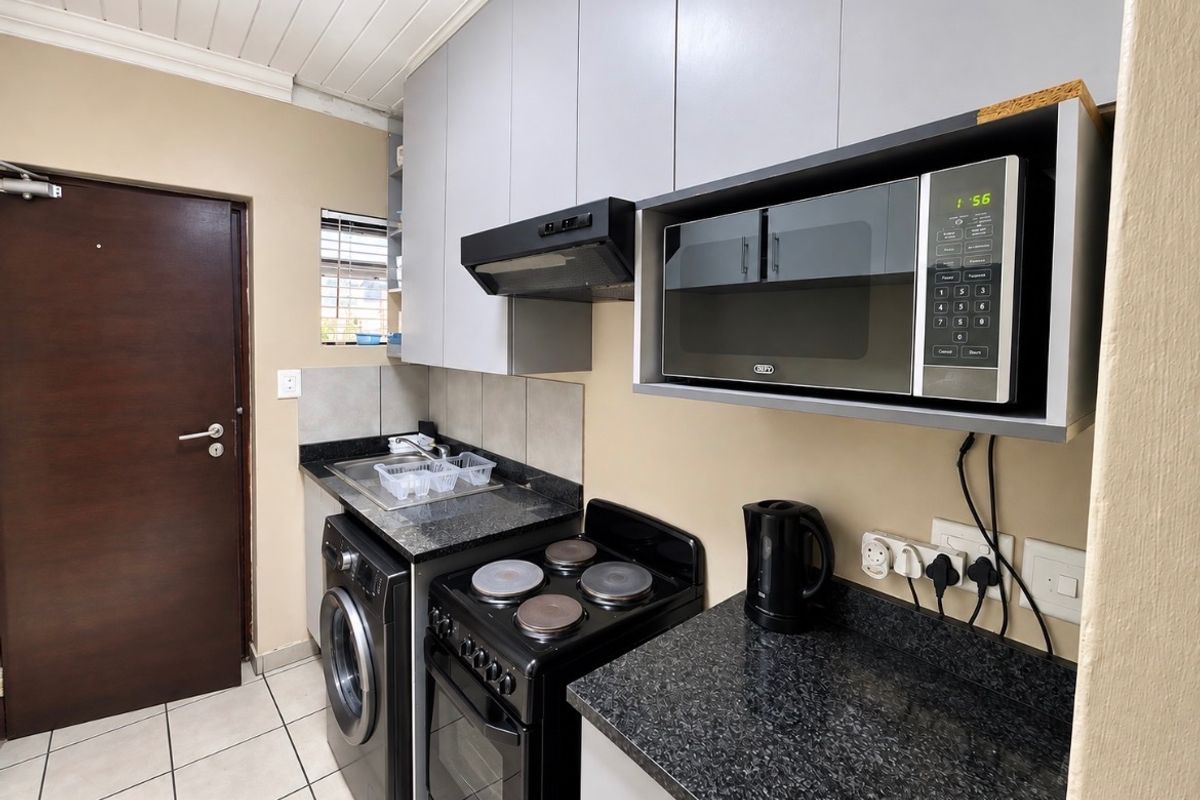 Compact kitchen featuring granite countertops, built-in cabinetry, an integrated microwave, extractor fan, and electric stove with tiled flooring.