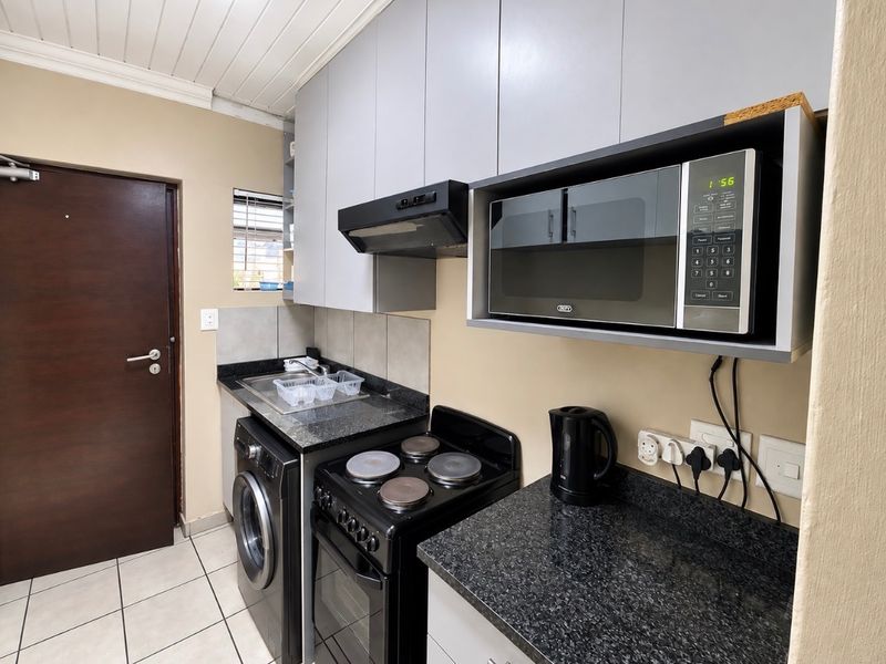 Compact kitchen featuring granite countertops, built-in cabinetry, an integrated microwave, extractor fan, and electric stove with tiled flooring.