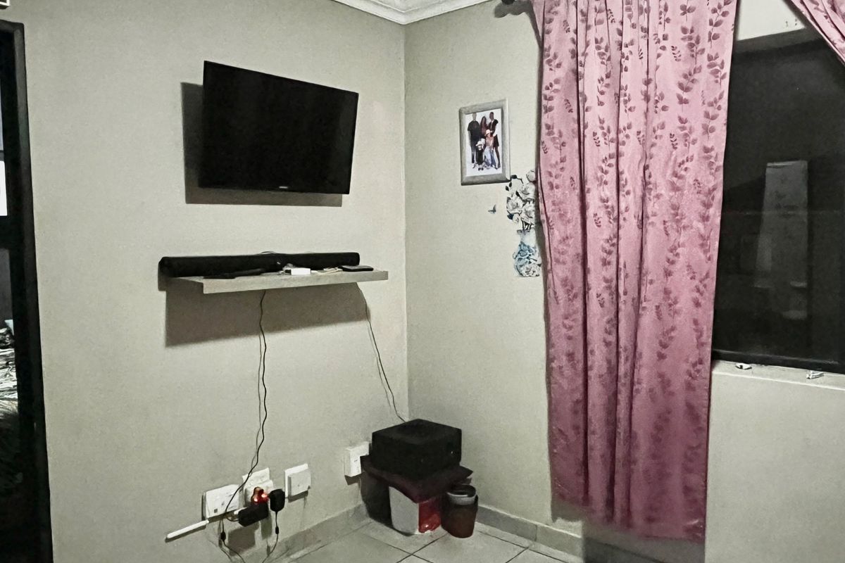 A living room area featuring tiled flooring, wall-mounted electrical points, and a window with curtains.