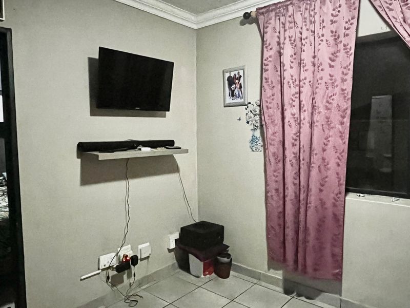A living room area featuring tiled flooring, wall-mounted electrical points, and a window with curtains.