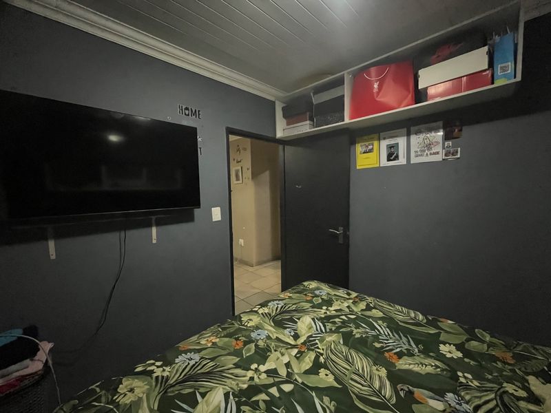 A bedroom featuring dark painted walls, built-in overhead storage shelving, and a timber panel ceiling with coving.
