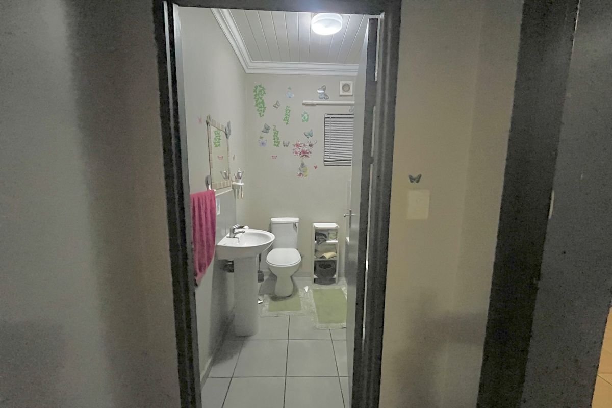 A functional bathroom featuring a pedestal basin, toilet, tiled flooring, and an extractor fan, viewed through a doorway.
