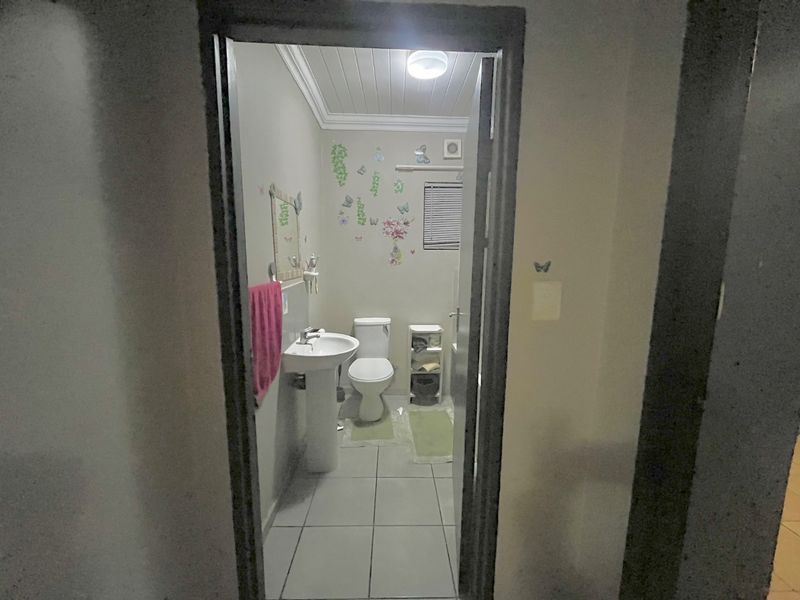 A functional bathroom featuring a pedestal basin, toilet, tiled flooring, and an extractor fan, viewed through a doorway.