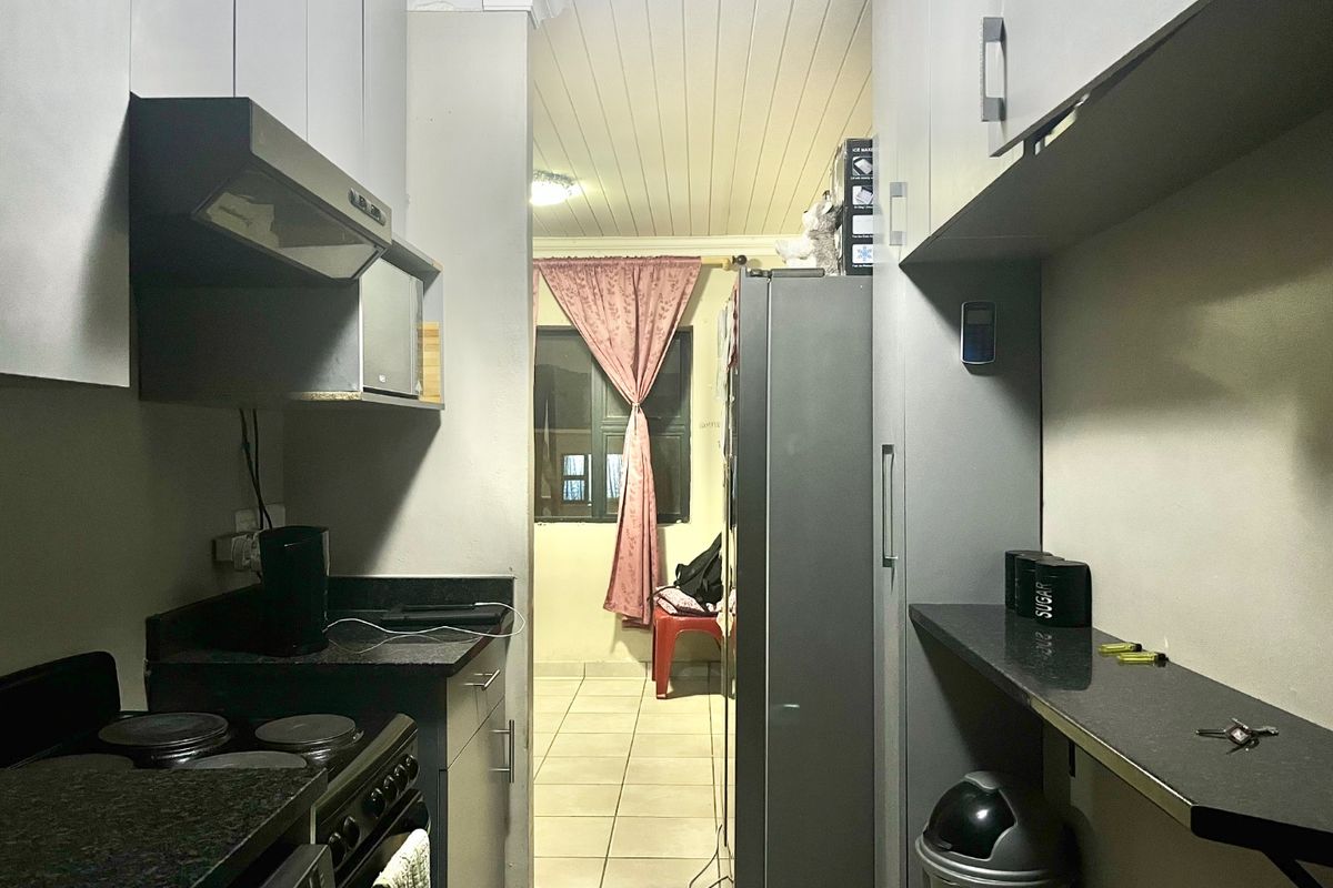 A functional galley-style kitchen featuring built-in cabinetry, granite countertops, and an integrated electric stove, leading into an adjacent living area.