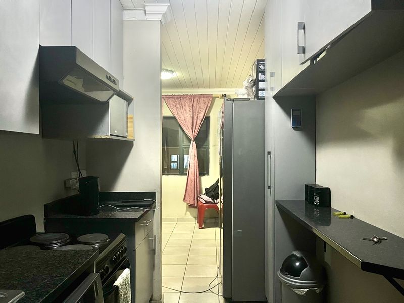 A functional galley-style kitchen featuring built-in cabinetry, granite countertops, and an integrated electric stove, leading into an adjacent living area.
