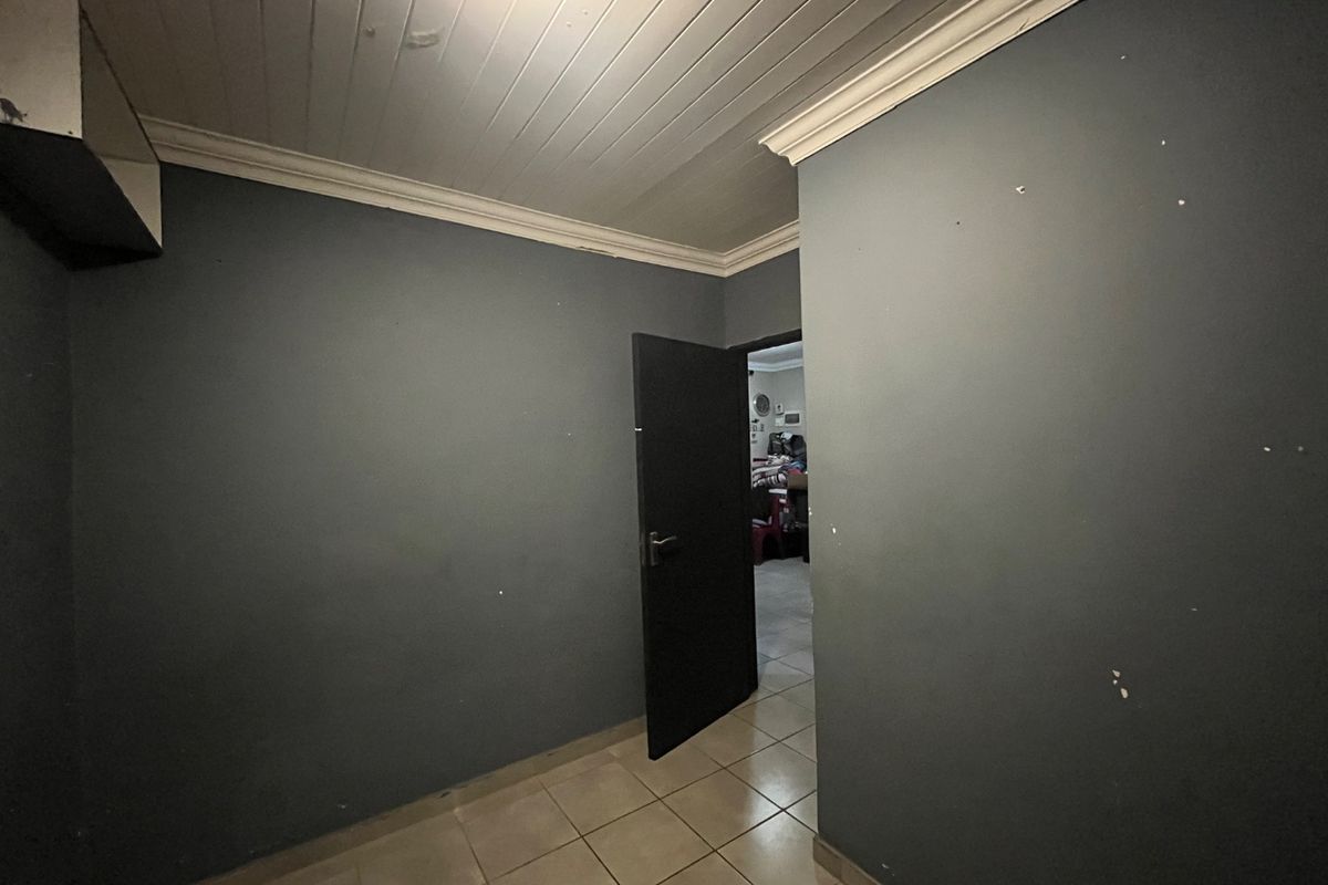 An empty bedroom featuring tiled flooring, a timber panelled ceiling, and dark grey walls requiring cosmetic attention.