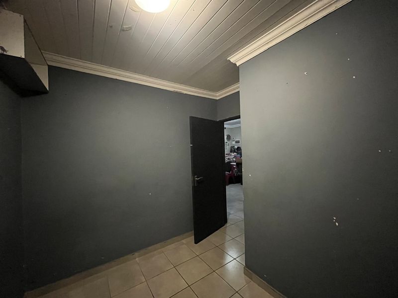 An empty bedroom featuring tiled flooring, a timber panelled ceiling, and dark grey walls requiring cosmetic attention.