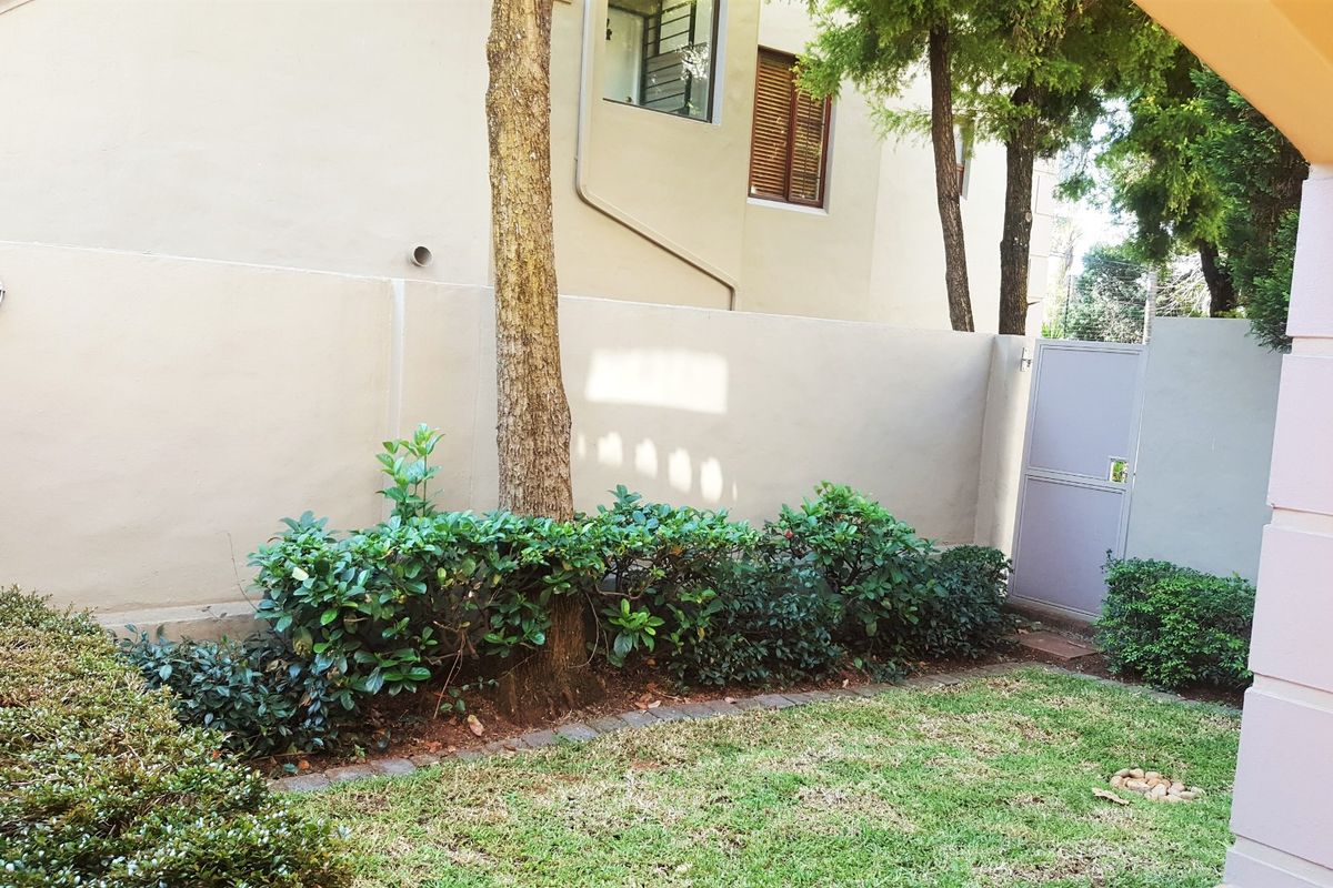 A private rear garden area featuring a well-maintained lawn, established shrubbery, a boundary wall, and a secure pedestrian gate.