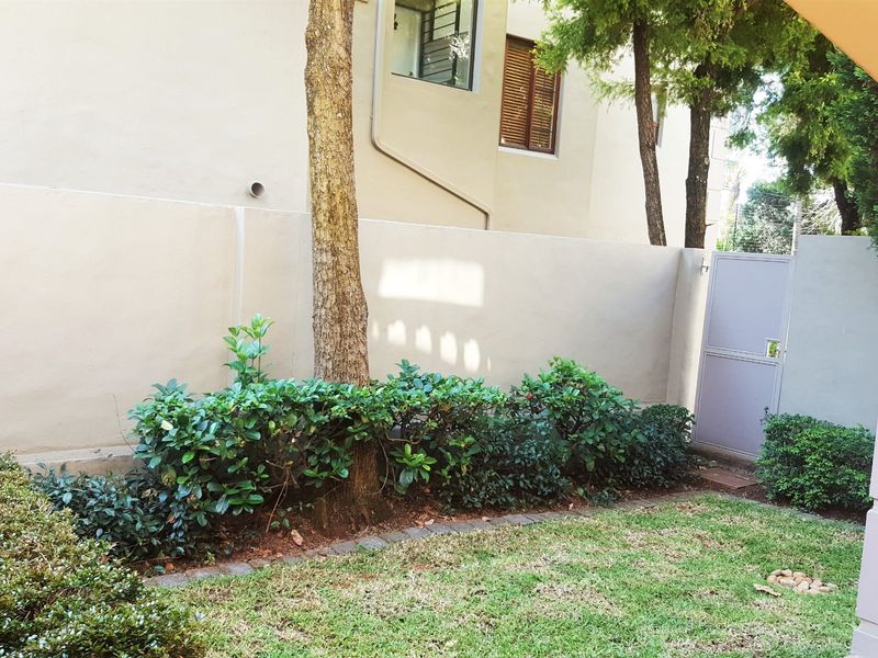 A private rear garden area featuring a well-maintained lawn, established shrubbery, a boundary wall, and a secure pedestrian gate.