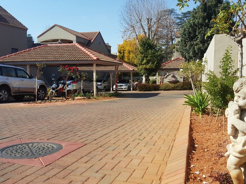 A view of the apartment complex driveway featuring covered parking bays, paved surfaces, and landscaped garden areas.