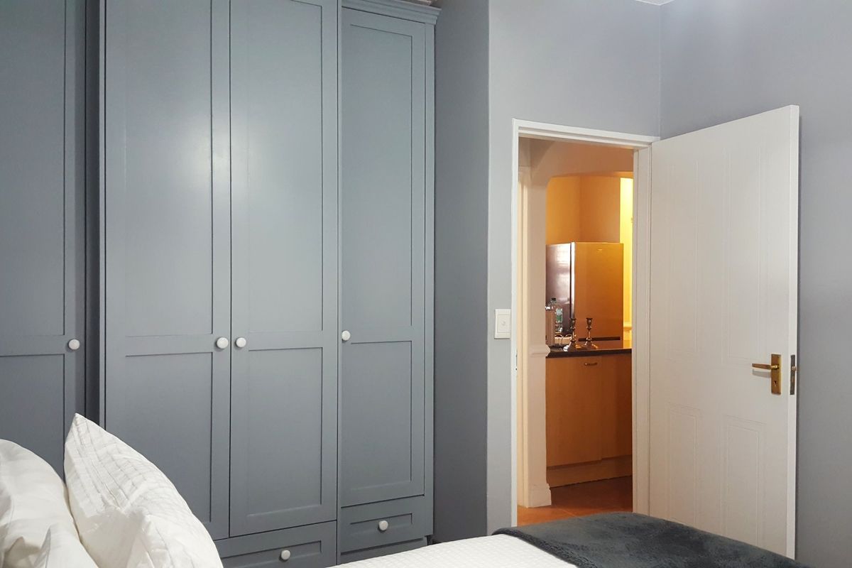 A bedroom featuring grey built-in cupboards with a view into an adjacent kitchen area.