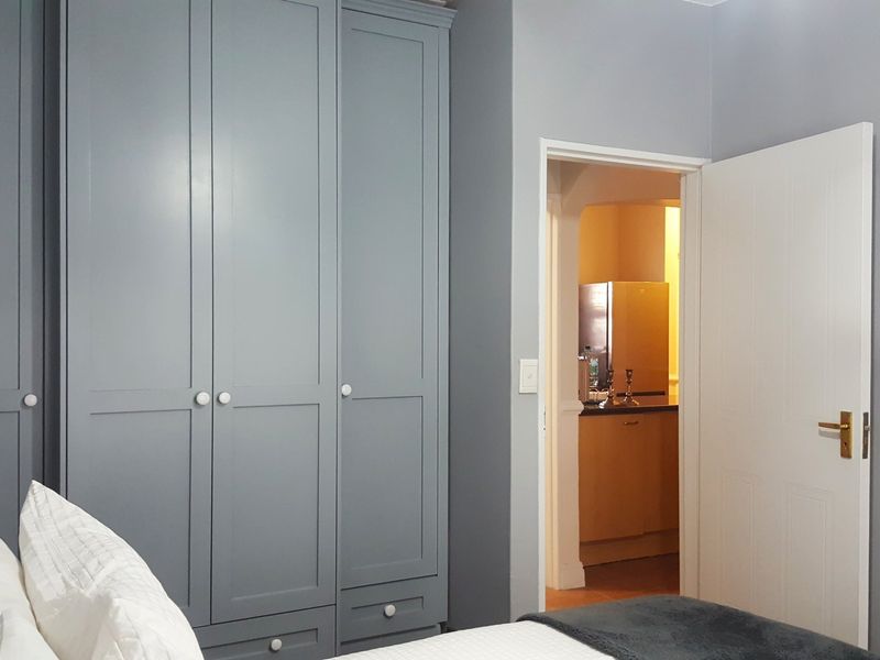 A bedroom featuring grey built-in cupboards with a view into an adjacent kitchen area.