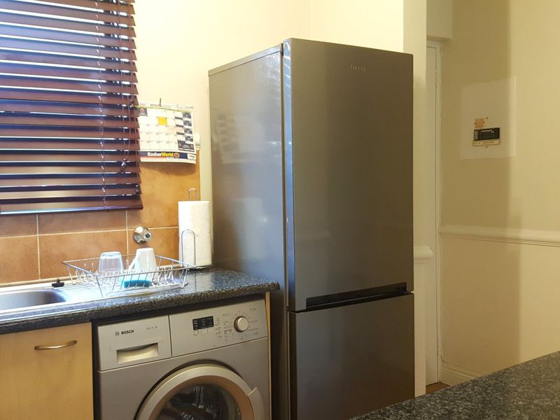 A functional kitchen area featuring a stainless steel sink, granite countertops, tiled splashback, and a built-in washing machine.