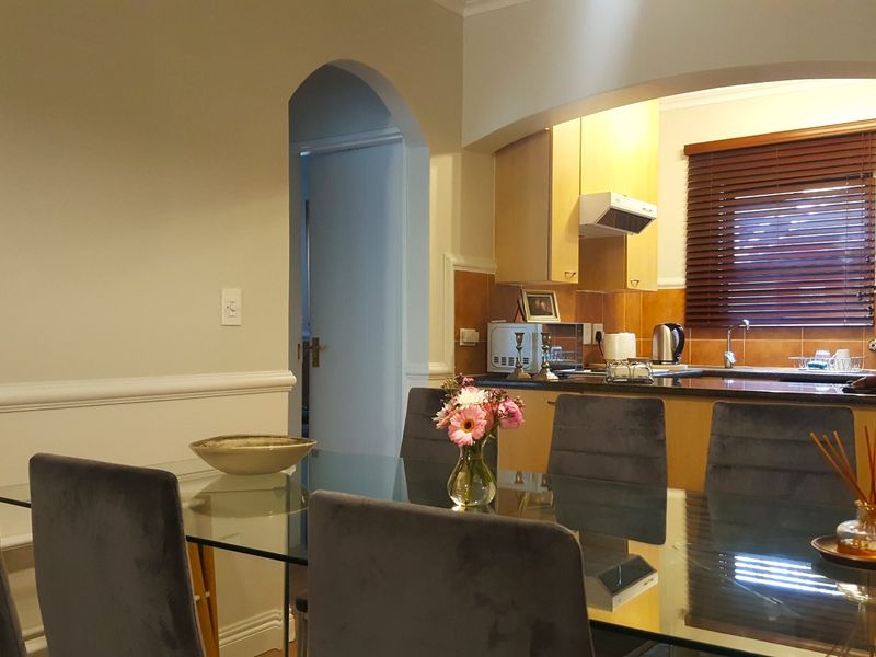Open plan dining area flowing into a functional kitchen with granite countertops, wooden cabinetry, and an arched entryway.