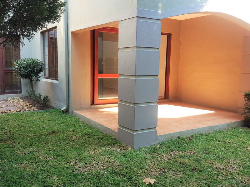 A covered patio area with tiled flooring and a masonry pillar, providing direct access to the surrounding garden space.
