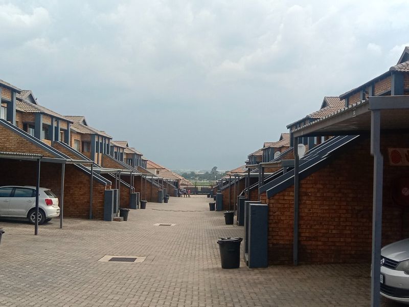 A view of a residential apartment complex featuring rows of brick-faced units with individual carports and a paved driveway.