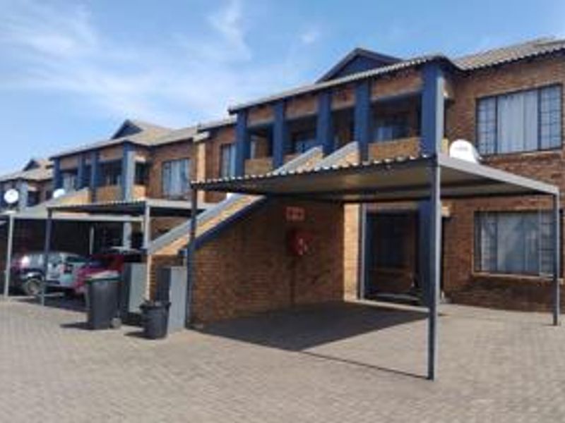Exterior view of a face brick apartment complex featuring covered parking bays and paved driveway access.