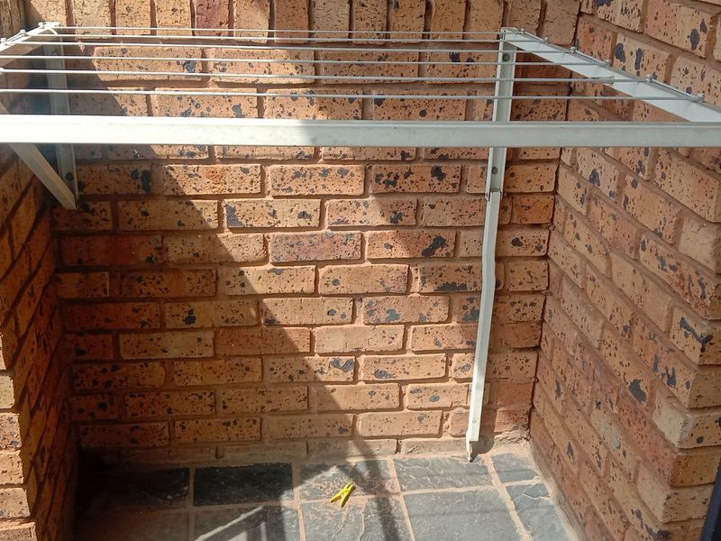 A functional balcony area featuring exposed brick walls, slate tile flooring, and a wall-mounted drying rack.
