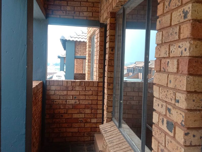 A covered balcony area featuring exposed brick walls and metal-framed windows, offering a view of the surrounding residential complex.