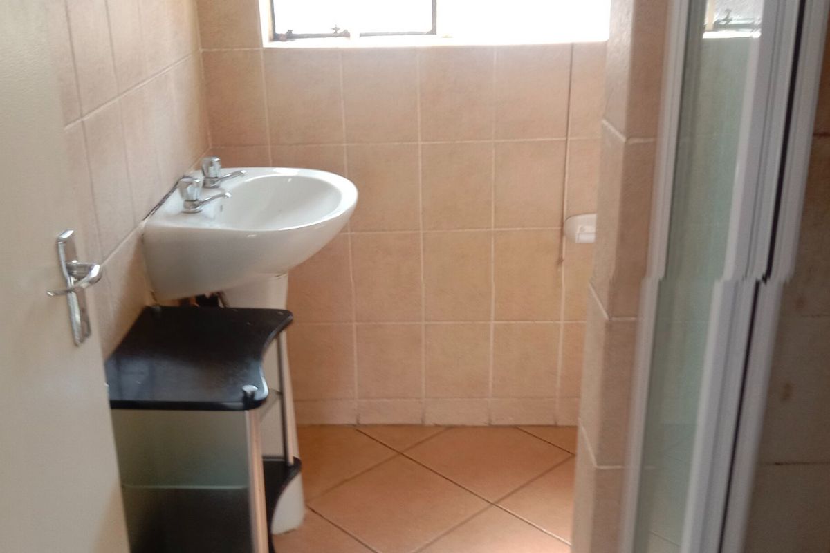 A functional bathroom featuring a pedestal washbasin, tiled walls and flooring, and a shower enclosure.