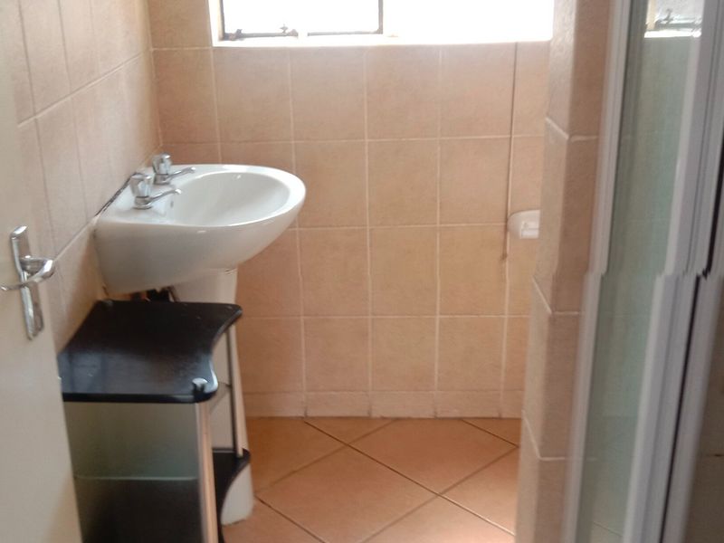 A functional bathroom featuring a pedestal washbasin, tiled walls and flooring, and a shower enclosure.
