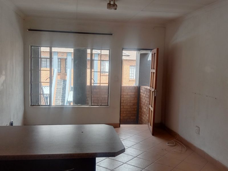 An empty open-plan living and kitchen area featuring tiled flooring, a built-in breakfast counter, and direct access to an outdoor balcony.