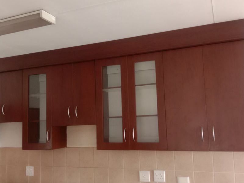 A kitchen area featuring dark wood built-in wall cabinetry with glass-fronted display sections and a neutral tiled backsplash.