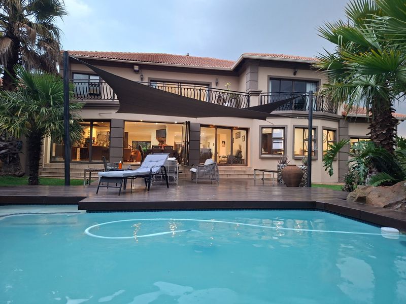 Rear view of the property featuring a swimming pool, timber decking, shade sail, and a spacious patio area with access to the main living space.