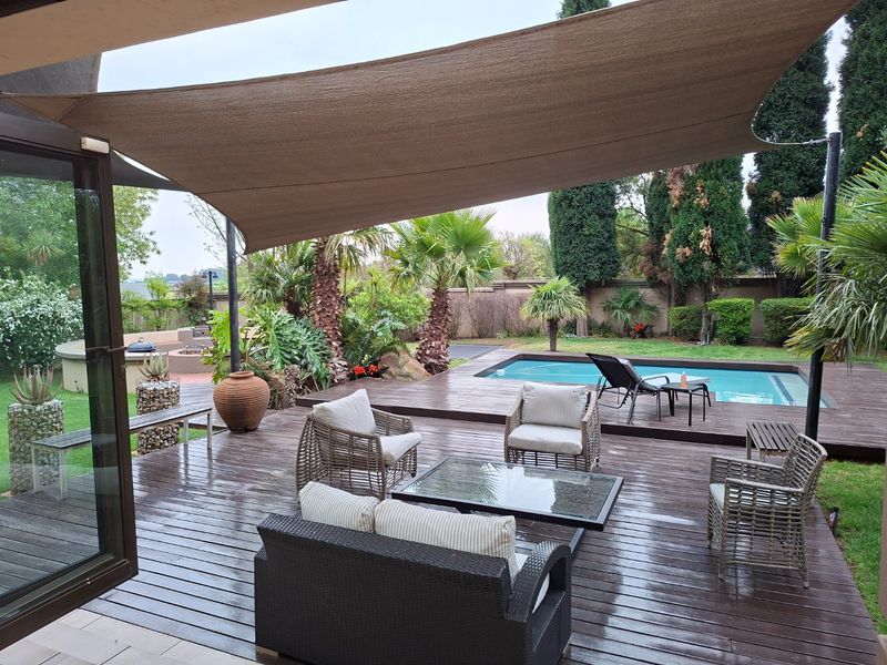 Outdoor entertainment area featuring a swimming pool, extensive timber decking, and a large shade sail, set within a landscaped garden.