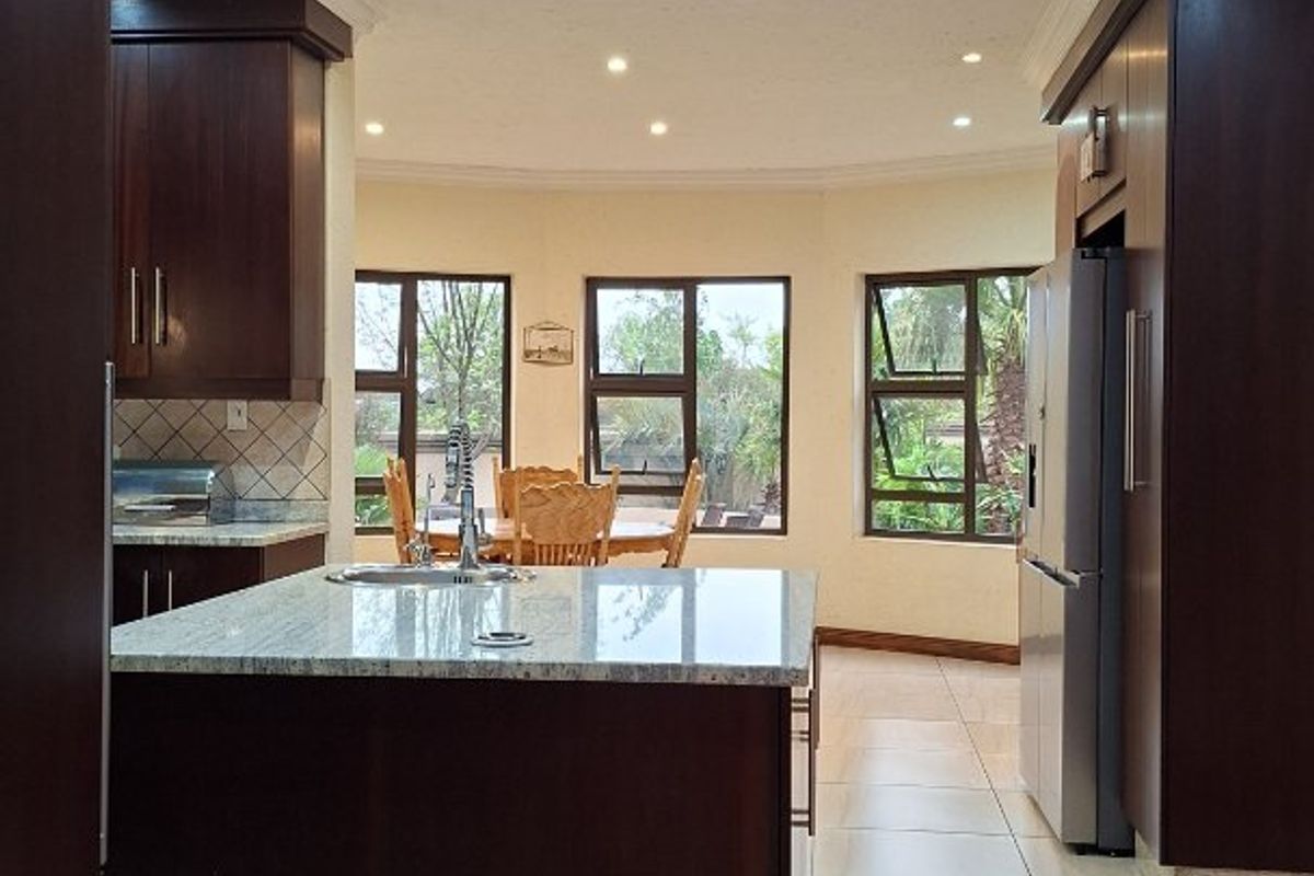 Spacious kitchen featuring dark wood cabinetry, granite countertops, a central island with sink, and large windows providing ample natural light.