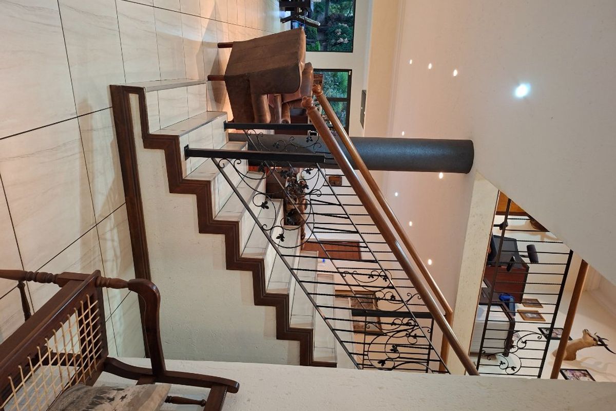 Spacious living area featuring a prominent staircase with a decorative wrought iron balustrade, wooden handrail, and modern recessed downlighting.