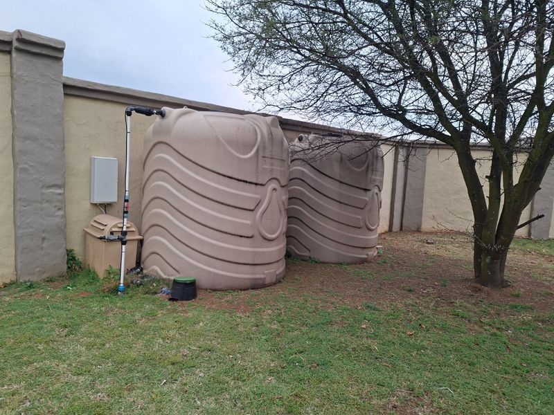 Rear garden area featuring two large plastic water storage tanks installed against a perimeter boundary wall with associated plumbing connections.