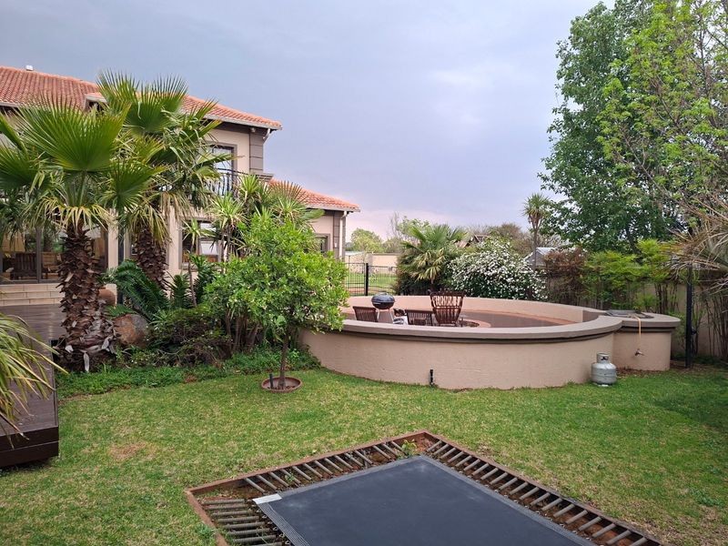 A spacious rear garden featuring a sunken fire pit area, wooden decking, and an in-ground trampoline, set against a well-maintained residential property.