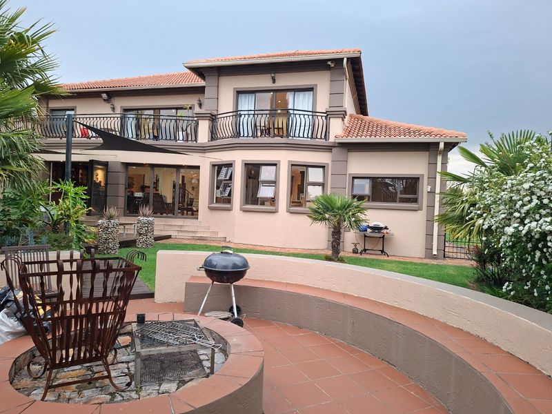 Rear view of a two-story house featuring a tiled patio with a built-in fire pit, curved seating, and an upper-level balcony with wrought iron railings.