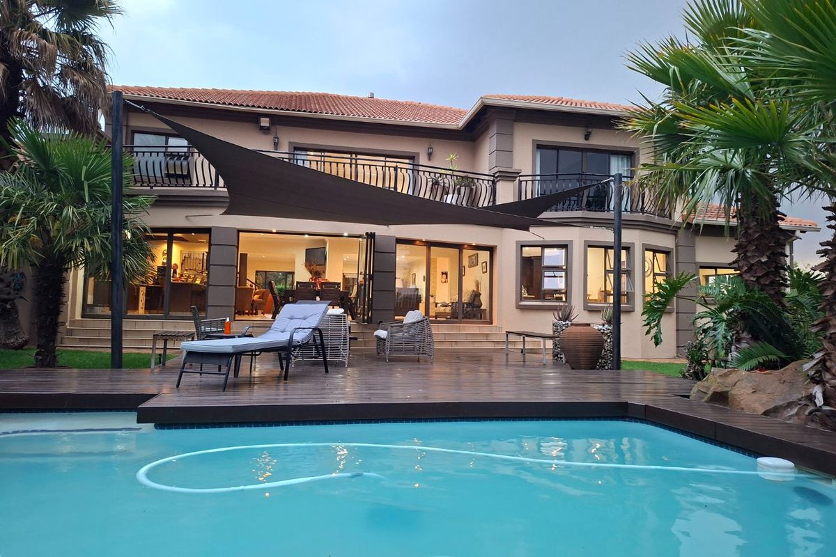 Rear view of a two-story house featuring a swimming pool, timber decking, and a covered patio area with balcony access.