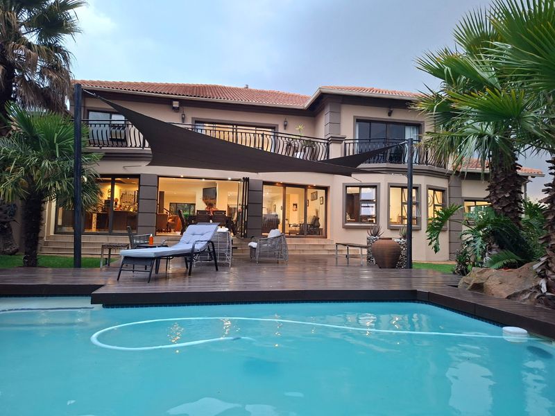 Rear view of a two-story house featuring a swimming pool, timber decking, and a covered patio area with balcony access.