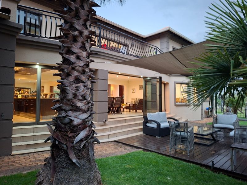 Rear view of the house featuring a tiled patio, wooden deck, shade sail, and an upper-level balcony with metal railings.