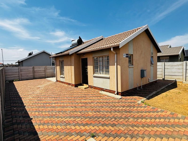 Rear view of a detached house featuring a paved courtyard, solar water heating system, and secure precast concrete perimeter walling.