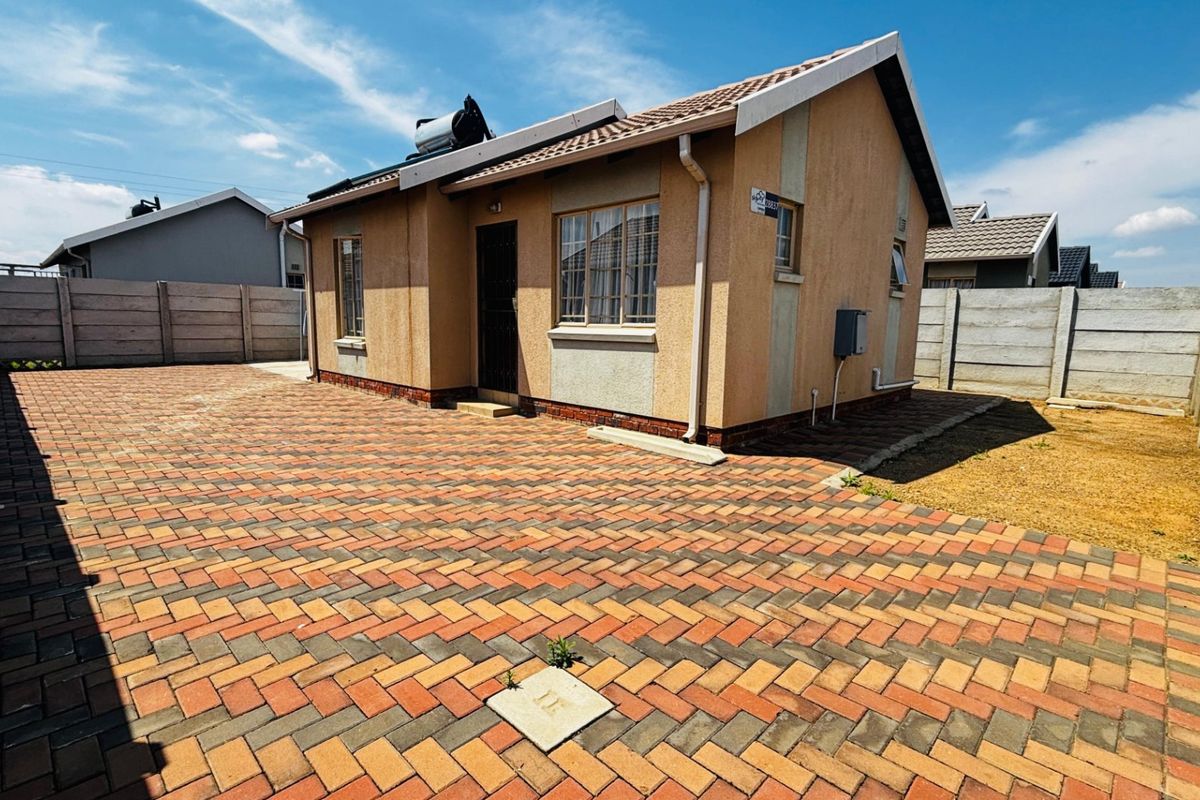 Rear view of a detached house featuring a paved courtyard, precast boundary walls, and a roof-mounted solar water heating system.