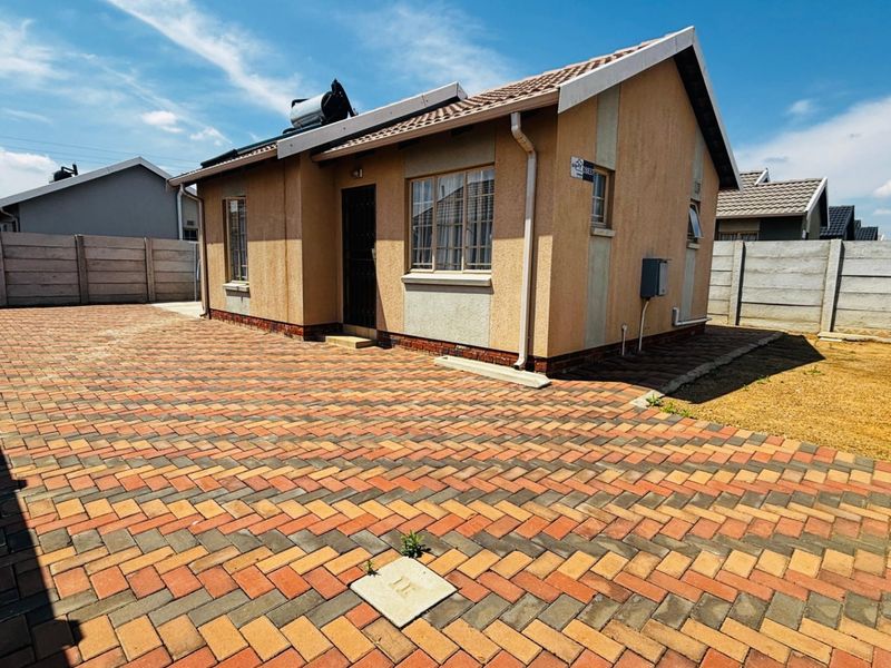 Rear view of a detached house featuring a paved courtyard, precast boundary walls, and a roof-mounted solar water heating system.